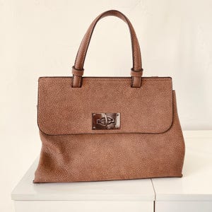 May include: A white ceramic mug with a black handle and the text "But First, Coffee" in a bold, black font. The mug is set against a blurred background, suggesting a cozy setting.