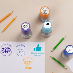 Pode incluir: Uma coleção de selos coloridos com várias mensagens, incluindo "WOW!", "Aprovado" e "Melhorar". Os selos são roxos, laranja e azuis, com bases cinzentas. Lápis e uma folha de papel com mensagens carimbadas também estão presentes.