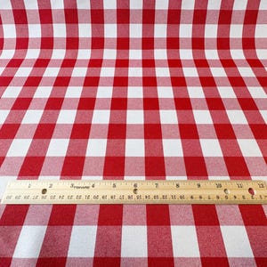 May include: Red and white checkered fabric with a wooden ruler placed across the bottom. The ruler is marked with both inches and centimeters. The fabric is curved, creating a sense of depth.