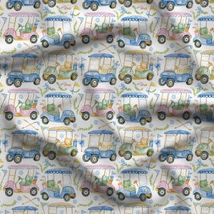 May include: A white fabric featuring a repeating pattern of watercolor-style golf carts in shades of blue, pink, and green. The design includes small illustrations of crossed golf clubs, flags, and blue polka dots scattered across the surface.