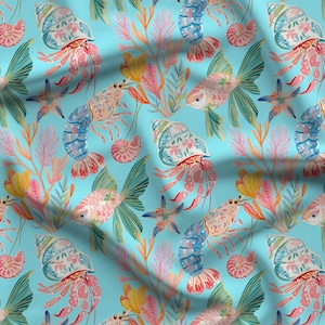 May include: A light blue fabric featuring a repeating pattern of pink hermit crabs in shells, orange and yellow coral, pink sea fans, starfish, and light pink fish with green fins. The bottom right corner displays the text AFP American Fabric Prints.