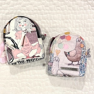 Puede incluir: Una taza de cerámica blanca con asa negra y el texto "But First, Coffee" en negrita negra. La taza se encuentra sobre un fondo borroso, sugiriendo un ambiente acogedor.