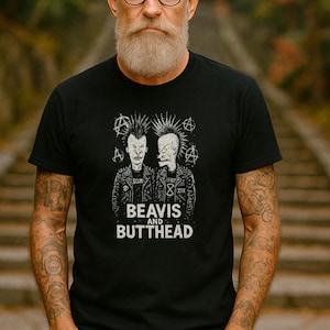 Puede incluir: Camiseta negra con un gráfico de Beavis y Butt-Head, personajes animados icónicos con pelo puntiagudo. El texto "BEAVIS AND BUTTHEAD" está impreso debajo de los personajes en blanco. La camiseta tiene cuello redondo.