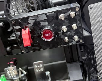 Peut inclure: Gros plan sur un panneau de contrôle noir avec un motif camouflage. Il comprend un bouton rouge 'ENGINE START' et plusieurs boutons argentés. Un interrupteur à bascule rouge est également visible. Il fait partie d'un système plus large.