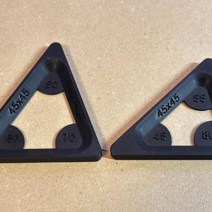 May include: Two black, triangular tools with rounded corners. Each tool has a 45x45 marking and circular cutouts with degree measurements. One has 50, 60, 70, and the other has 45, 55, 80 degree markings.