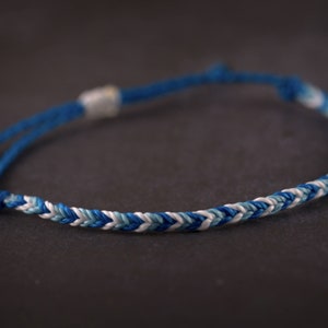 May include: A blue and white braided friendship bracelet with a white knot at the end.