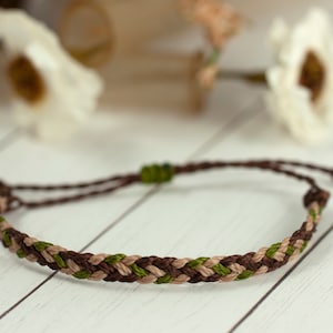 May include: A brown, beige, and green braided friendship bracelet with adjustable closure.