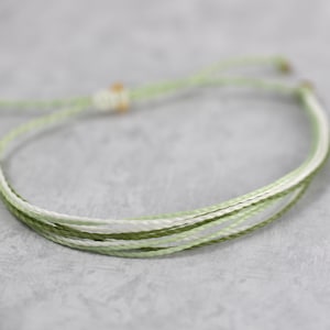 May include: A green and white braided bracelet with a simple knot closure.