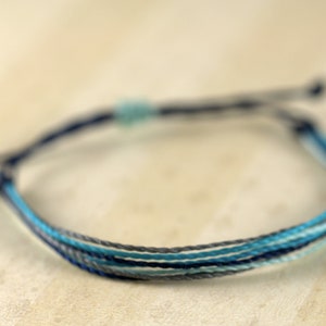May include: A multi-colored friendship bracelet with blue, gray, and white threads.