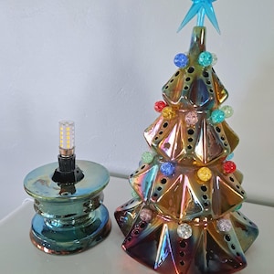 May include: Iridescent ceramic Christmas tree with a blue star topper and colorful bead ornaments. A matching iridescent lamp base with a light bulb is next to the tree. The tree has a metallic finish.