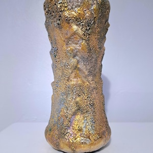 May include: A textured, handcrafted vase with a unique, organic design. The vase features a blend of gold, bronze, and iridescent hues, creating a striking visual effect. The vase has a wide base and a slightly flared top, standing approximately 8 inches tall.