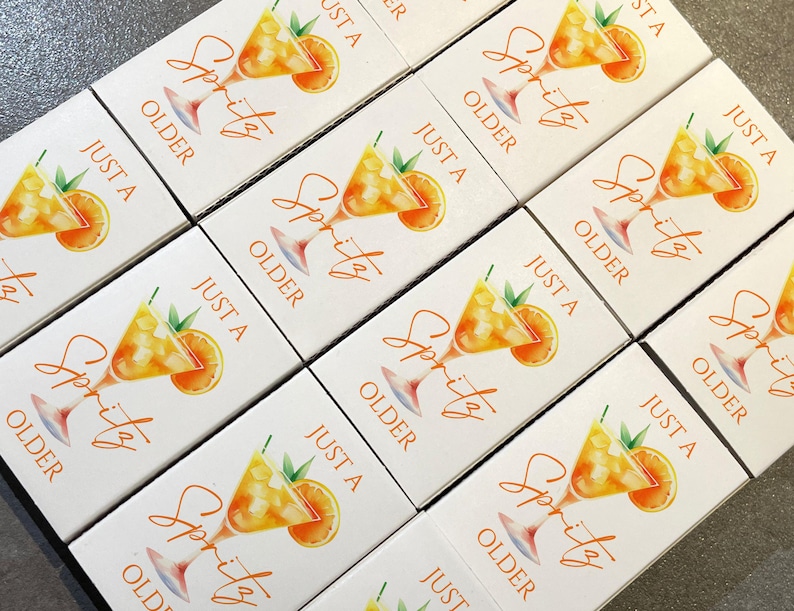 May include: White boxes with a watercolor illustration of a spritz cocktail, an orange slice, and text that reads "Just a Spritz Older". The boxes are arranged in a grid pattern.