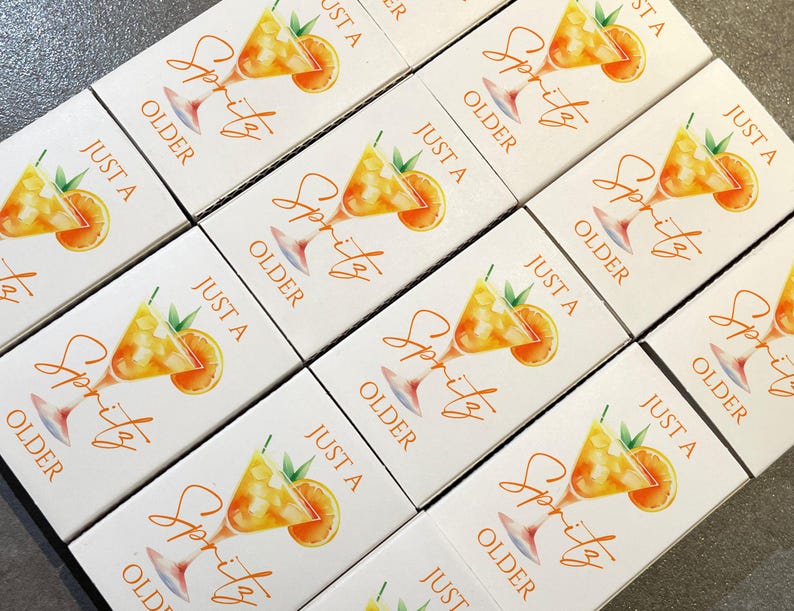 May include: White boxes with a watercolor illustration of a spritz cocktail, an orange slice, and text that reads "Just a Spritz Older". The boxes are arranged in a grid pattern.