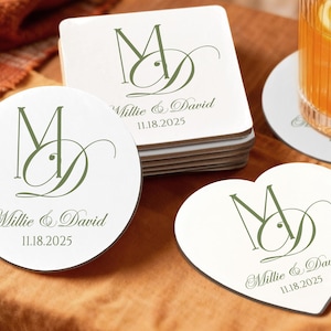 May include: White coasters in round, square, and heart shapes, featuring a green monogram design with the names "Millie & David" and the date "11.18.2025". The coasters are stacked and arranged on a brown surface.