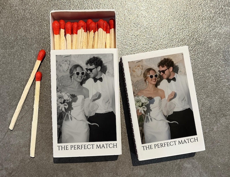 May include: A white matchbox with a black and white photo of a couple wearing sunglasses, with the text "THE PERFECT MATCH". The matchbox is open, revealing red-tipped matches. Two loose matches are next to the box.