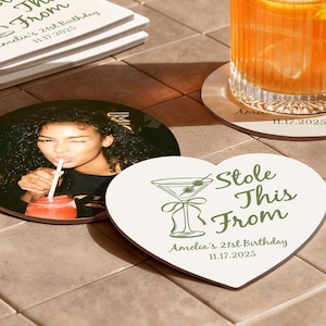 May include: A collection of personalized coasters. One round coaster features a photo of a woman drinking a beverage. A heart-shaped coaster and other round coasters have a martini glass graphic and text that reads "Stole This From Amelia's 21st Birthday 11.17.2025."