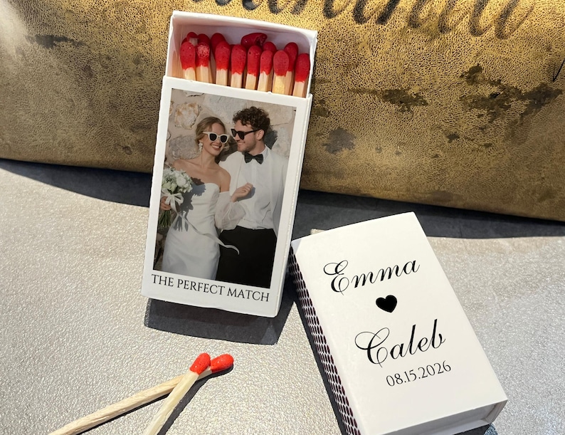 May include: A white matchbox with a photo of a couple and the text "THE PERFECT MATCH." The matchbox is open, revealing red-tipped matches. A second matchbox is open, with the names "Emma" and "Caleb," a heart, and the date "08.15.2026."