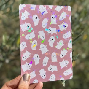 May include: A rectangular sticker featuring a repeating pattern of small white ghosts with smiling faces on a dusty pink background, accented with scattered holographic geometric shapes that reflect light in various colours.