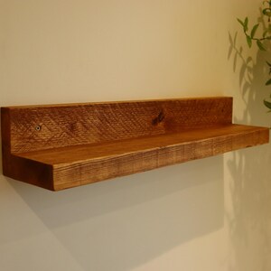 May include: A rustic wooden shelf with a natural brown finish. The shelf is mounted to a white wall and has a simple, minimalist design.