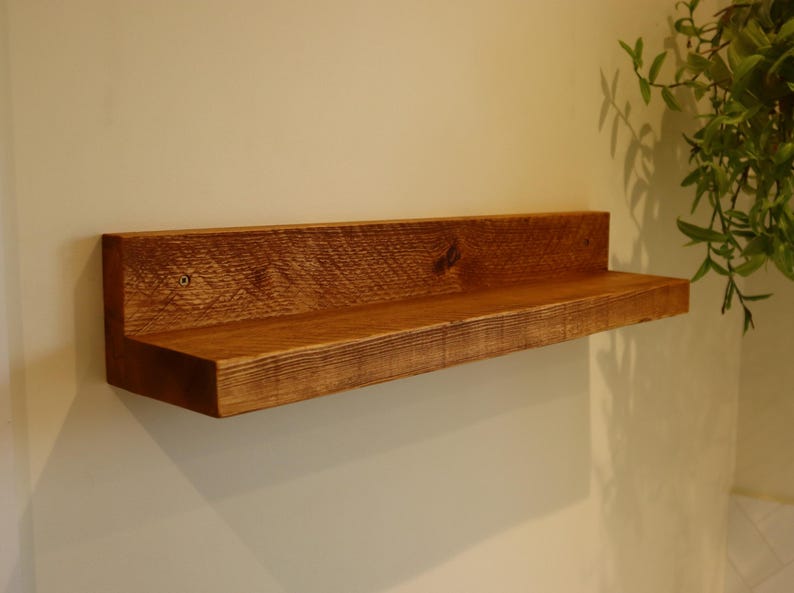 May include: A rustic wooden shelf with a natural brown finish. The shelf is mounted to a white wall and has a simple, minimalist design.