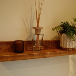 May include: A rustic wooden shelf with a brown finish, featuring a clear glass diffuser with wooden sticks, a dark brown candle, and a white ceramic planter with a green plant.
