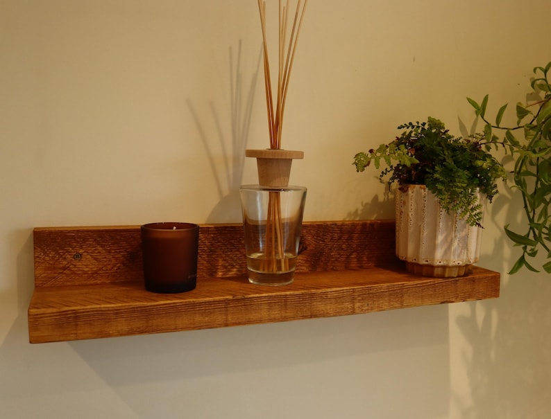 May include: A rustic wooden shelf with a brown finish, featuring a clear glass diffuser with wooden sticks, a dark brown candle, and a white ceramic planter with a green plant.