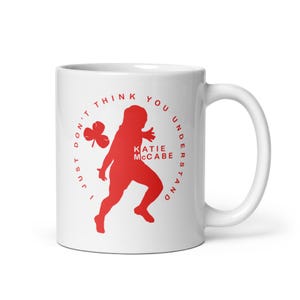 Könnte beinhalten: Weiße Keramiktasse mit roter Grafik einer rennenden Person, einem Kleeblatt und dem Text "I JUST DON'T THINK YOU UNDERSTAND KATIE McCABE". Die Tasse hat einen gebogenen Henkel und eine glänzende Oberfläche.