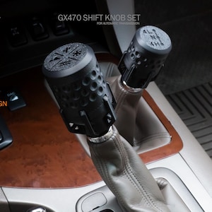 May include: A set of two black shift knobs for a car. The knobs have a textured surface and are labeled with the letters "4HL" and "4L". The knobs are installed on a car's gear shifter.