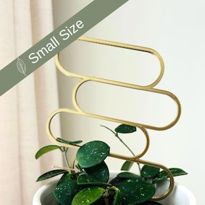 Peut inclure: Support de plante en métal doré avec un design ondulé et abstrait. Le support est dans un pot blanc avec une plante verte qui pousse à l'intérieur.