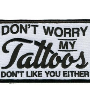May include: A rectangular white patch with black embroidered text. The text reads "DON'T WORRY MY Tattoos DON'T LIKE YOU EITHER". The patch has a black border.