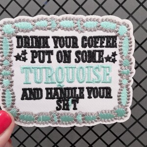May include: A rectangular embroidered patch with a white background and a decorative border in turquoise and grey. The text reads: DRINK YOUR COFFEE, PUT ON SOME TURQUOISE, AND HANDLE YOUR SH*T, with black lettering and a turquoise word for emphasis.