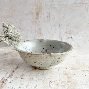 May include: A white ceramic mug with a black handle and the text "But First, Coffee" in a black, handwritten-style font. The mug is on a white surface.