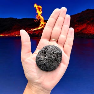 Può includere: Una roccia lavica porosa grigio scuro è tenuta in una mano aperta. La roccia ha una superficie ruvida e strutturata con molti piccoli fori. Lo sfondo mostra un lago blu e un'eruzione vulcanica infuocata.
