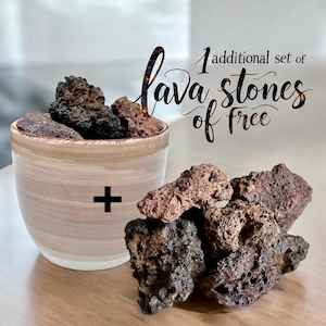 Puede incluir: Un conjunto de piedras de lava marrones y negras en un cuenco de cerámica beige con un signo más en el lateral. El texto "1 additional set of lava stones of free" está escrito en cursiva negra sobre un fondo blanco.