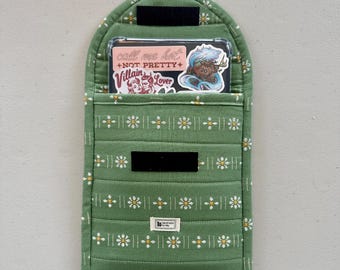 Op de afbeelding: Groen stoffen telefoonhoesje met een wit madeliefjespatroon. Het hoesje heeft een transparant plastic venster met een sticker waarop staat "Call me hot, not pretty" en een andere sticker met een vrouwengezicht en de woorden "Villain Lover".