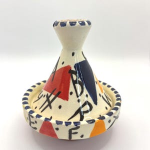 Peut inclure: Un petit tagine en céramique blanche avec un couvercle conique. Le couvercle est décoré de formes géométriques en rouge, bleu et orange. La base du tagine est décorée d'une bande bleu et blanche.