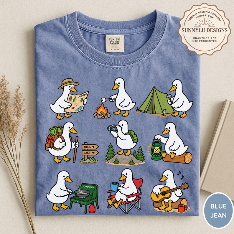 May include: A blue crew neck t-shirt featuring a graphic print of nine white ducks engaged in various camping activities, including reading a map, roasting a marshmallow, setting up a tent, hiking, using binoculars, holding a lantern, cooking, sitting in a chair, and playing guitar.