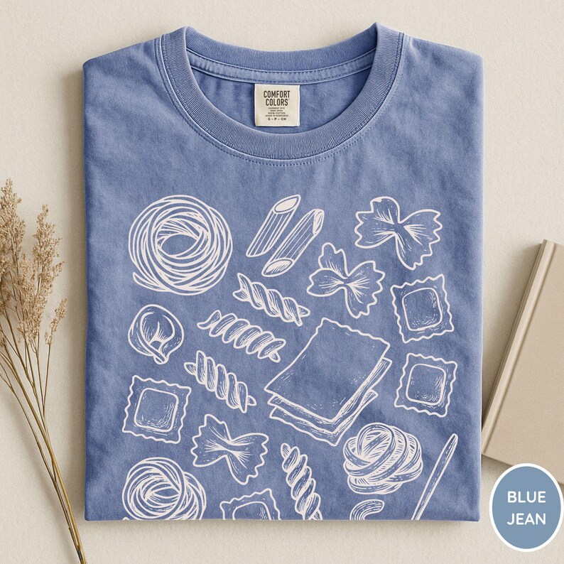 Puede incluir: Una camiseta color azul jean con un estampado gr&aacute;fico de l&iacute;neas blancas de varias formas de pasta, incluyendo farfalle, ravioli, penne y l&aacute;minas de lasa&ntilde;a. La camiseta tiene cuello redondo y una etiqueta de la marca Comfort Colors en el cuello.