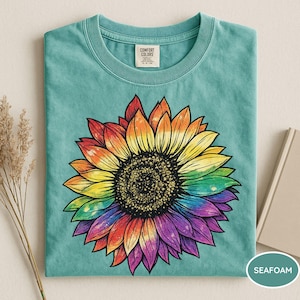 May include: A seafoam green short-sleeve t-shirt featuring a large, central graphic of a sunflower with petals transitioning through a rainbow spectrum of colors, including red, orange, yellow, green, blue, and purple, with a dark brown center.