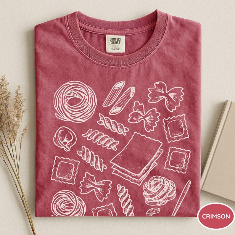 Puede incluir: Una camiseta de manga corta color carmes&iacute; con un estampado gr&aacute;fico de l&iacute;neas blancas de varias formas de pasta, incluyendo penne, farfalle, raviolis y l&aacute;minas de lasa&ntilde;a. La etiqueta interior del cuello muestra la marca Comfort Colors.