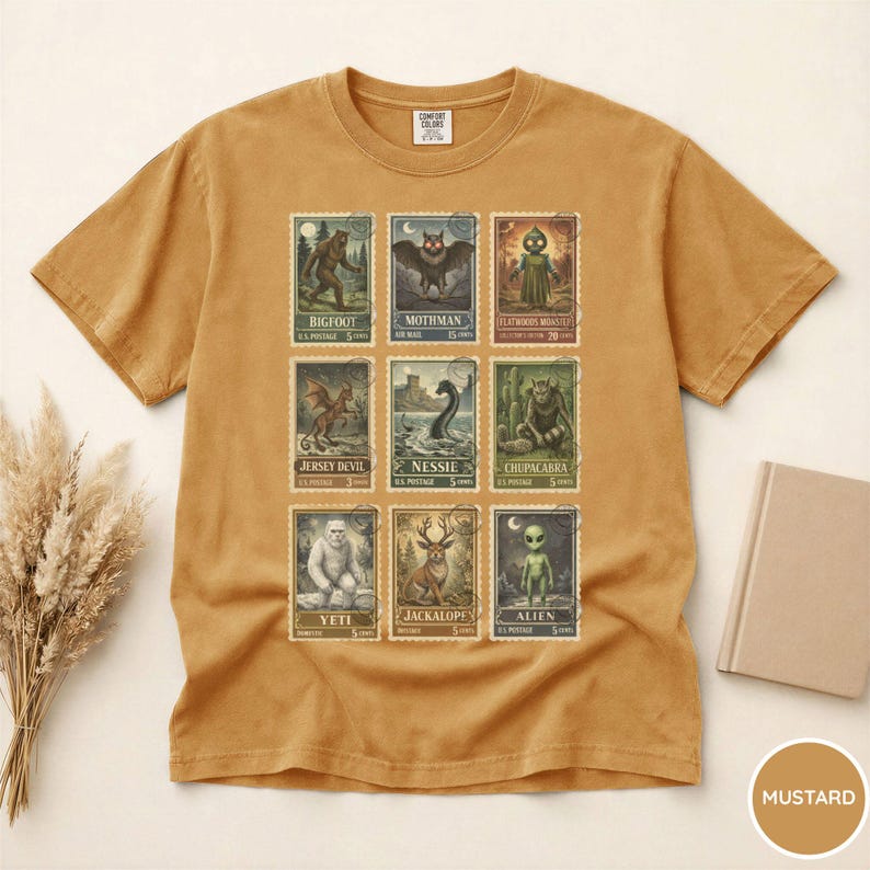 May include: Mustard-colored t-shirt featuring a collection of cryptid-themed postage stamp designs. The stamps depict creatures like Bigfoot, Mothman, and Nessie. The shirt has a classic crew neck and short sleeves, made of a soft, comfortable material.