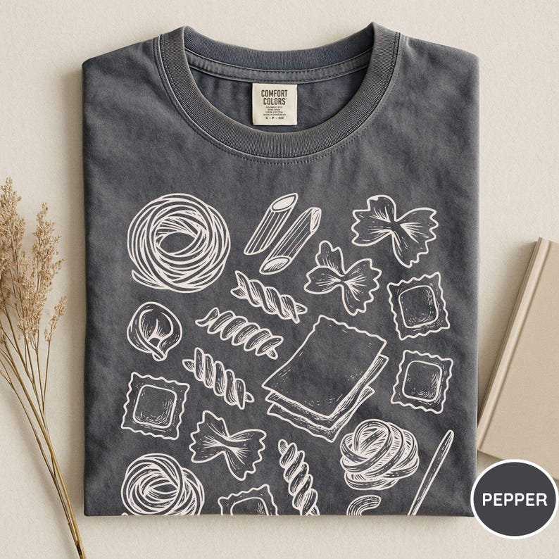 Puede incluir: Una camiseta de cuello redondo en color gris carb&oacute;n con un estampado gr&aacute;fico de l&iacute;neas blancas que muestra varias formas de pasta, incluyendo penne, farfalle, raviolis y l&aacute;minas de lasa&ntilde;a. Incluye la etiqueta de la marca Comfort Colors en el cuello.