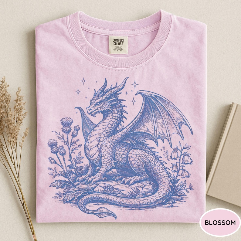 Peut inclure: T-shirt rose clair avec un dessin bleu d'un dragon ail&eacute;, entour&eacute; de fleurs et d'&eacute;toiles. Le t-shirt est &eacute;tiquet&eacute; "Blossom" et porte une &eacute;tiquette Comfort Colors.