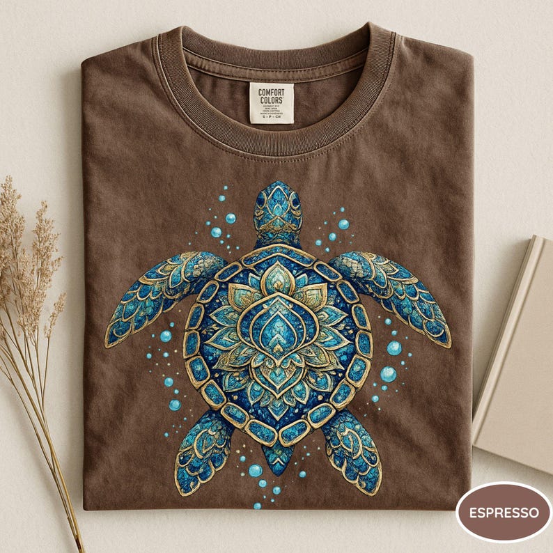 May include: A brown short-sleeve t-shirt featuring a central graphic of a sea turtle with a blue and gold mandala-style shell pattern. The turtle is surrounded by small blue bubbles. The inner neck label displays the text Comfort Colors.