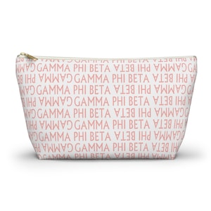 Peut inclure: Trousse de maquillage blanche avec un motif répété des mots "GAMMA PHI BETA" en rose clair. Le sac est doté d'une fermeture éclair dorée.