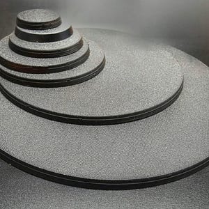 May include: A set of five circular, flat, black discs of varying diameters stacked in a stepped, spiral arrangement. Each disc features a textured, matte surface finish and thin, defined edges, creating a layered, geometric structure.