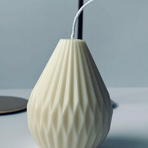 May include: A white pear-shaped candle with a geometric pattern. The candle has a white wick.