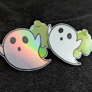 May include: Two ghost stickers, one iridescent and one white, with green accents. The iridescent ghost has a surprised expression, while the white ghost has a neutral expression.