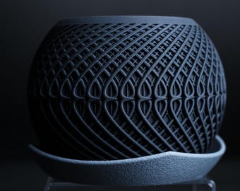 May include: A black ceramic planter with a geometric pattern and a grey saucer. The planter has a unique, intricate design.