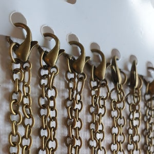 Può includere: Primo piano di sette catene dorate con chiusura a moschettone. Le catene sono disposte verticalmente e sono tutte della stessa lunghezza.